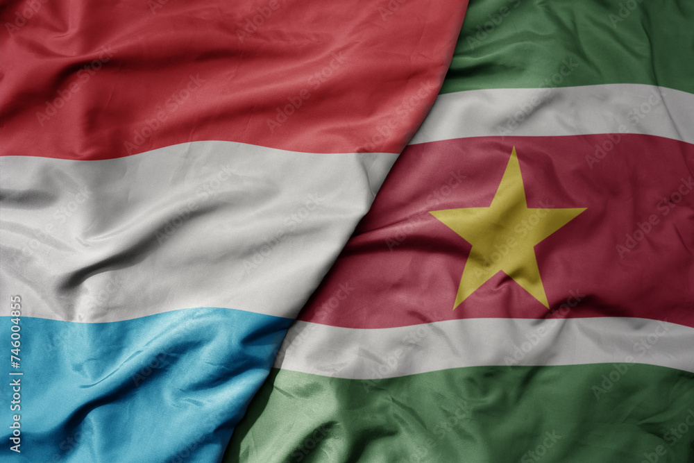 big waving national colorful flag of suriname and national flag of luxembourg .