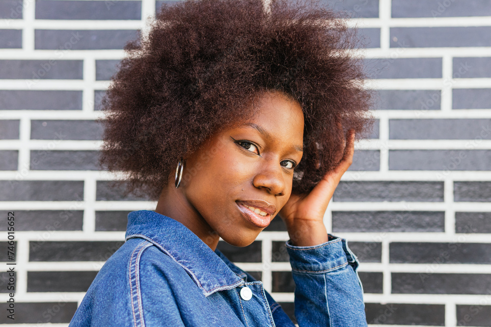 Stylish African American woman gives a confident side glance, her natural hair contrasting with the graphic urban brick wall behind her Stylish African American woman gives a confident side glance, her natural hair contrasting with the graphic urban brick wall behind her