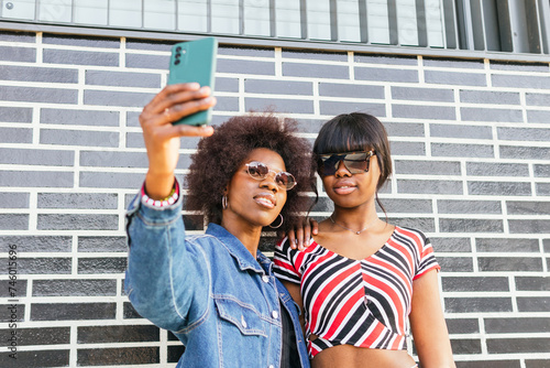 Two sisters are taking a selfie, capturing a moment of their vibrant urban life together against a striking brick wall photo