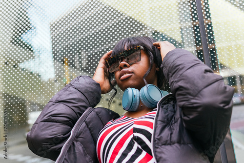 From below of young woman finds joy in music, her oversized headphones creating a personal haven against the drizzly cityscape