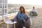 Beautiful adult African American female discussing agreement using smartphone while doing outdoor office work, businessman colleague working on blurred background.