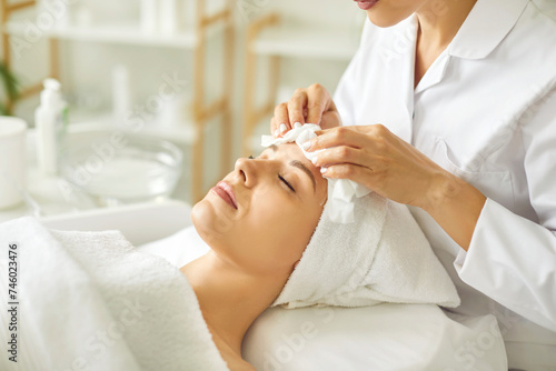 Quadro su tela Close-up photo pf professional cosmetologist or beautician doctor hands making anti-age procedures cleaning with napkins facial mask of young pretty woman client in beauty spa clinic