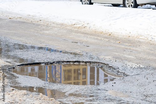 pothole on an asphalt road with a puddle during the spring or winter thaw. poor quality road surface