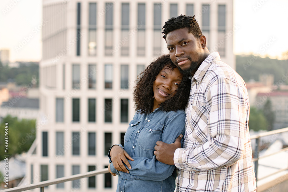Concept of love relationships and outdoors activity. Young African American couple woman and man hugging on rooftop of modern building and looking at camera.