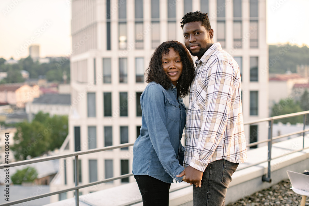 African American people in love waking at evening on rooftop of modern building. Young girlfriend and boyfriend having date after work. Urban portrait of loving couple.