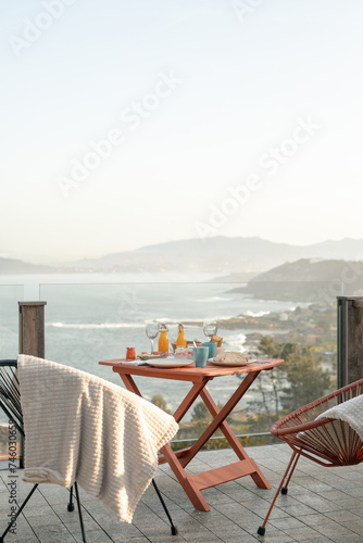 Outdoor breakfast table with sea view during sunrise. Warm morning light with copy space. Cozy seaside dining and leisure concept for design and print