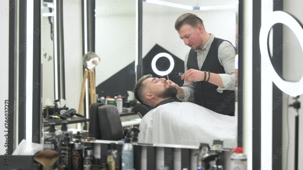 A barber trims a Caucasian clients mustache with a trimmer. A barber trims a Caucasian clients mustache with a trimmer.