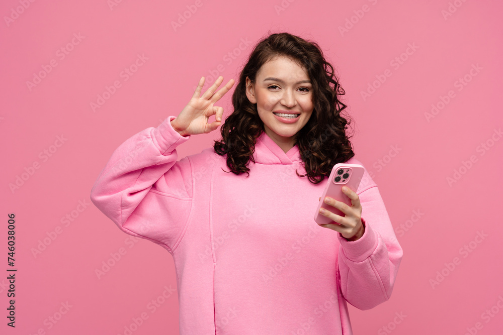 happy smiling woman in pink hoodie posing on pink studio background holding smartphone happy smiling woman in pink hoodie posing on pink studio background holding smartphone