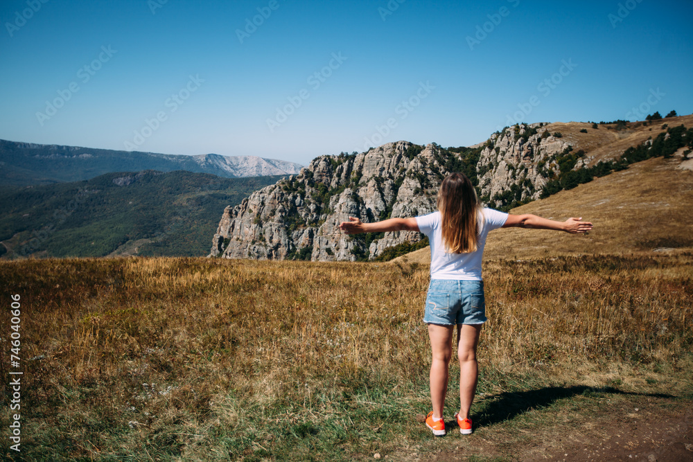 The girl spread her arms to the side and lifted her head up against the background of the mountain landscape. Mountain hiking. A walk through the mountains