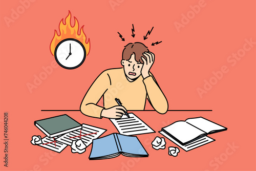 Excited man student is writing thesis and panicking because of deadline, sitting at table near burning clock. Guy student needs help filling out application or test for admission to university.