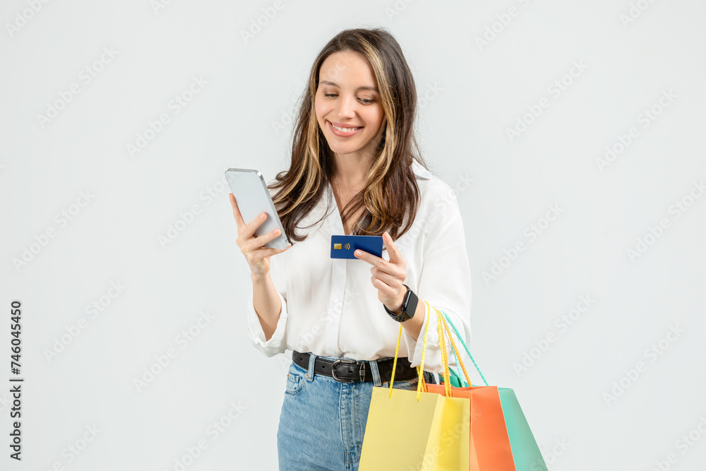 Happy young woman in a white blouse and blue jeans, holding a credit card and looking at her smartphone Happy young woman in a white blouse and blue jeans, holding a credit card and looking at her smartphone