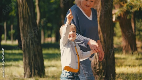 Cute little boy and his grandmother walking in park together, happy childhood photo