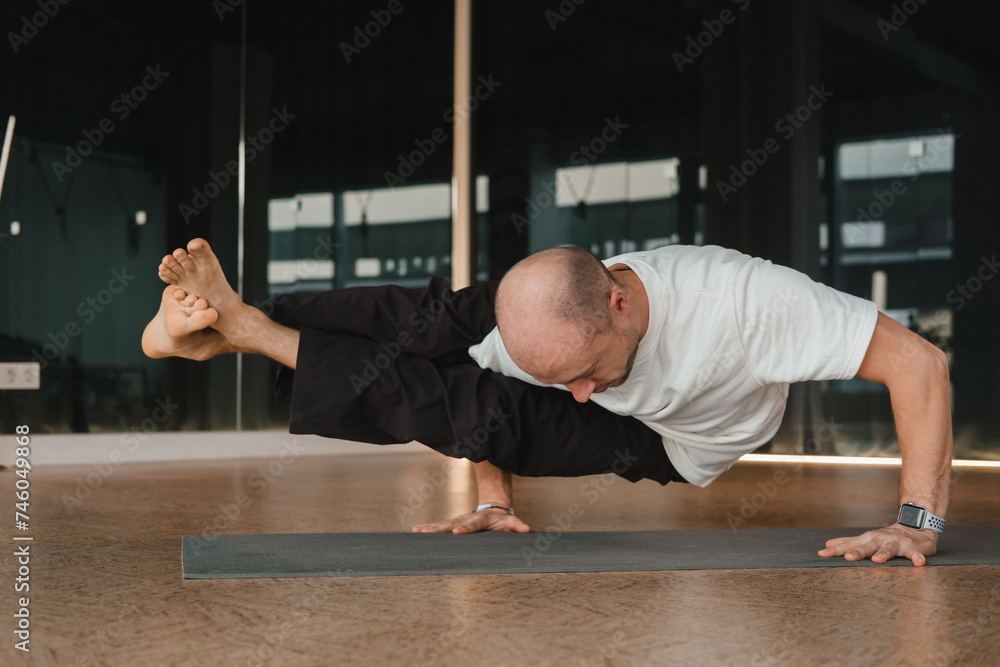 An athletic young man does exercises in the fitness room. A professional guy does yoga in the gym