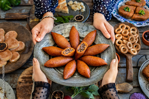 Hands of two women holding kibbeh plate . Turkish name is oruk or içli köfte or icli kofte . Dinner table with many meals on the table.   photo