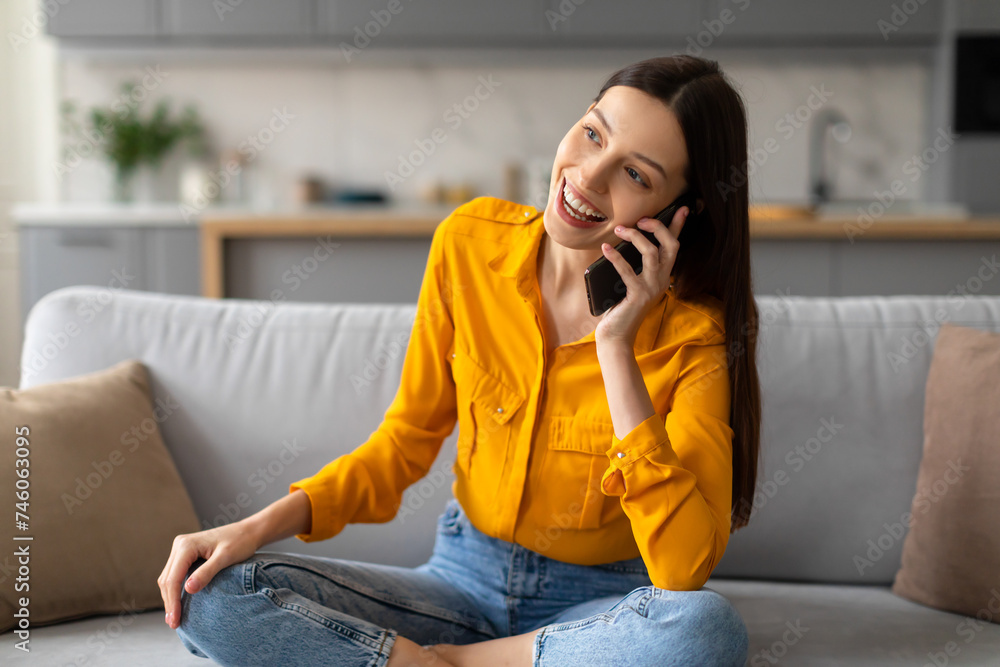 Happy woman chatting on phone, relaxed on couch