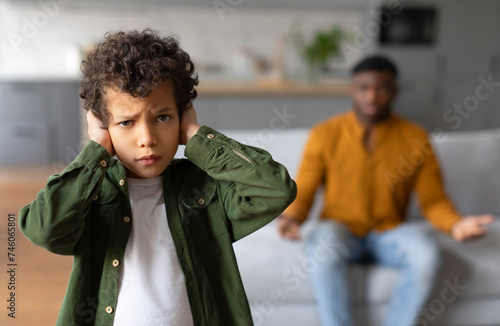 Black child boy covering ears with parent arguing on background