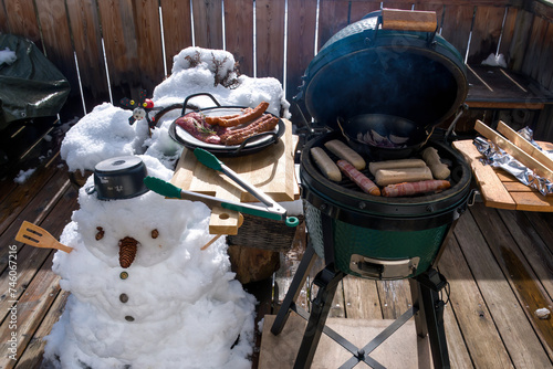 bbq - cooking outdoor on a charcoal grill at a cold sunny winter day with fresh snow and a snowman
