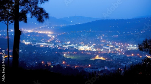 a view of a city at night from a hill with a lot of lights on the buildings and trees in the foreground.