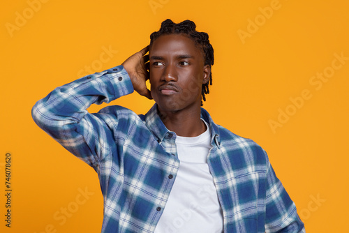 Pensive young black man touching his head and looking away thoughtfully