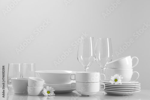 Set of many clean dishware, flowers and glasses on light table. Space for text