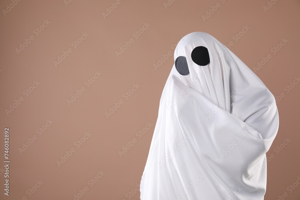 Creepy ghost. Person covered with white sheet on dark beige background, space for text