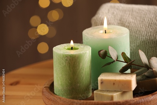 Spa composition. Burning candles, soap, towel and eucalyptus branch on wooden table, space for text