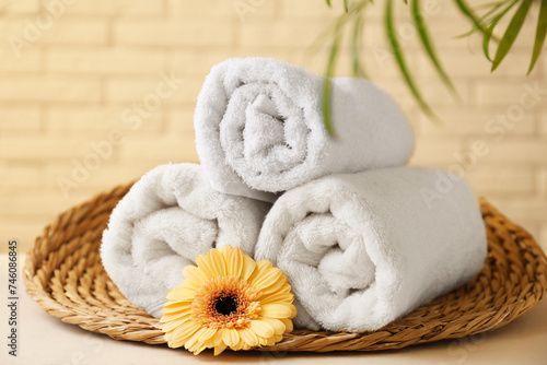 Rolled terry towels, flower and green leaves on white table near brick wall indoors, closeup