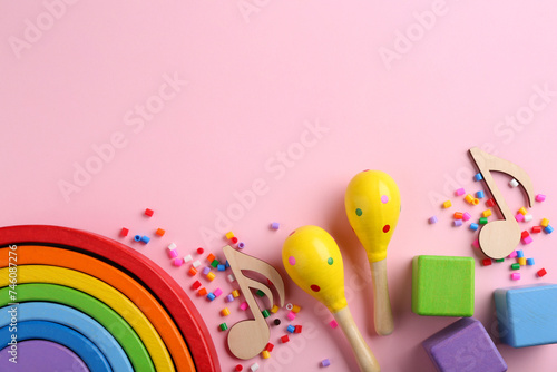Baby song concept. Wooden notes, kids maracas and toys on pink background, flat lay. Space for text