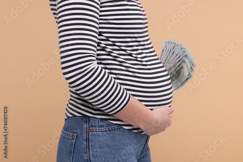 Surrogate mother. Pregnant woman with dollar banknotes on beige background, closeup