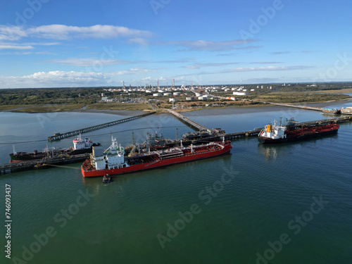 Three oil tankers moored at Fawley oil terminal. Fawley oil refinery and fuel storage tanks in the morning sun. Aerial view of biggest UK oil refinery with oil terminal.
