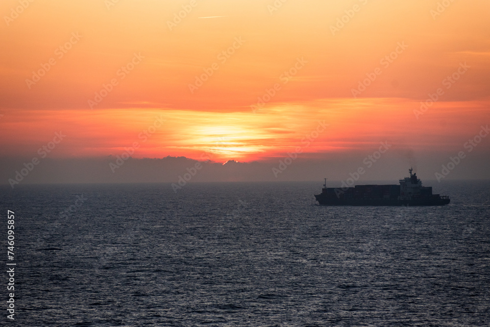 Sunset sky over the calm ocean -  
silhouette of the cargo ship on her lonely journey. 