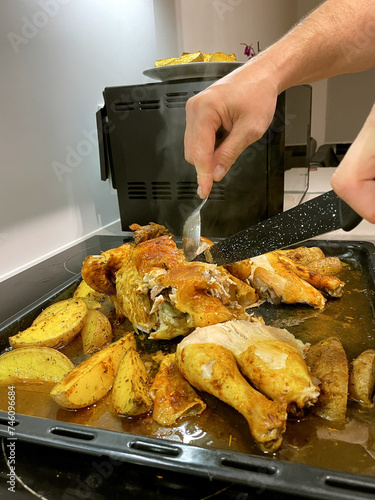 Hands cut baked chicken with potatoes with a knife.