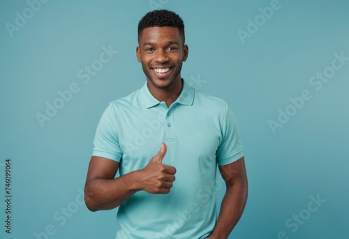 A man wearing a turquoise polo shirt smiles as he gives a thumbs-up, his relaxed demeanor and casual attire reflect an easygoing personality.