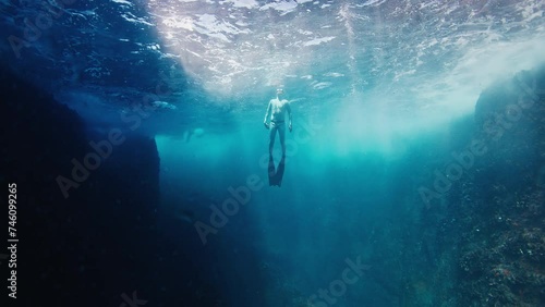 Freediver swims underwater in the sea and ascends near the rock photo