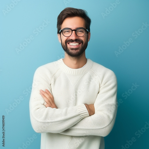 Young handsome man with beard wearing casual sweater and glasses over blue background happy face smiling with crossed arms looking at the camera. Positive person.
