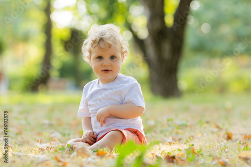 Cute curly blond baby sitting on the grass in autumn