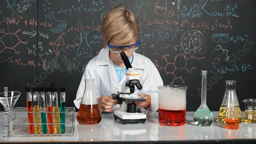 Smart boy using microscope analysis sample at science laboratory in STEM science class or chemistry lesson. Happy caucasian student looking under scope to inspect chemical liquid in tubes. Erudition.