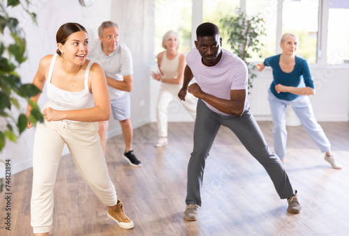 Group of positive young and aged people engaged in sport dances in training room during workout session