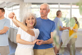 Positive senior woman and man practicing tango dance moves as a couple during a group celebration in a dance studio