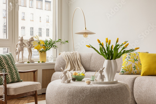 Interior design of spring living room with design sofa, furniture, vase with tulips, easter decorations, pillows and personal accessories. Home decor. Template. Easter holidays. photo