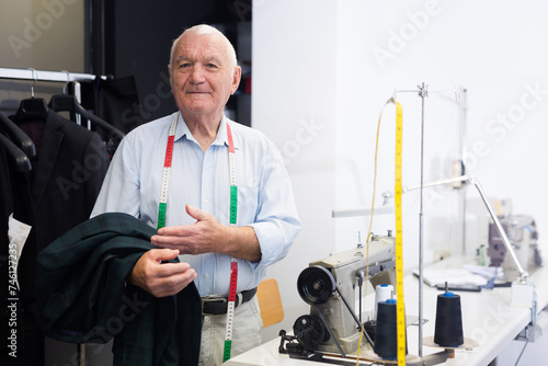 Senior man tailor posing next to sewing machine in sewing atelier