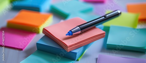 A pen is seen sitting atop a sheet of colorful sticky note paper. The paper is covered in various Post-It notes, and the pen is placed neatly on the top sheet.
