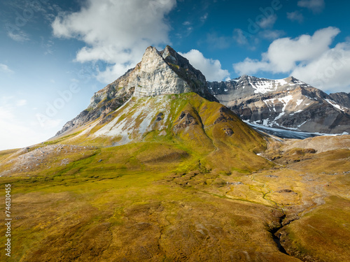 drone shot of majestic mountains in the heights in the middle of a sunny day surrounded by clouds, wild nature in svalbard, useful for magazines and magazines, traveling for mountains, svalbard