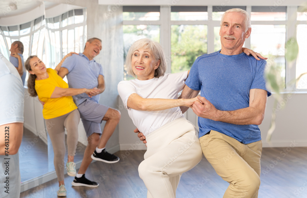 Obraz premium Enthusiastic senior couple, woman and man in sportswear, participating in group class for aged people, practicing energetic upbeat jive. Social dancing concept..