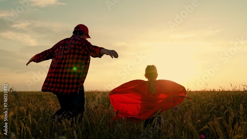 Dad child run around in red raincoats, playing outdoors. Family carnival in field, Parent kid. Dad of daughter plays superheroes in wheat field. Dad, girl dreams of becoming superhero, fly in red cape