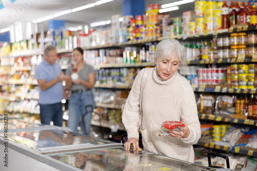 Elderly woman choosing frozen food in supermarket. Young woman purchasing goods in grocery store © JackF