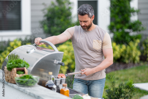 Cropped image of handsome man is making grill barbecue outdoors on the backyard. Bbq party. Bbq meat, grill for picnic. Roasted on barbecue. Man preparing barbeque in the house yard.