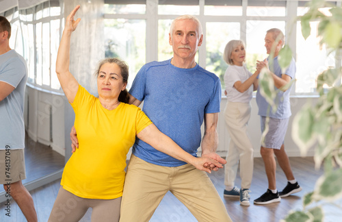 Happy smiling elderly woman enjoying impassioned merengue with male partner in latin dance class. Social dancing concept..