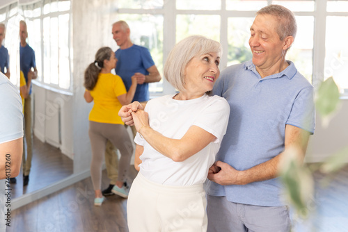 Happy smiling elderly woman enjoying impassioned merengue with male partner in latin dance class. Social dancing concept..