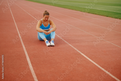 Athlete woman sitting on a running track at the stadium and relaxing